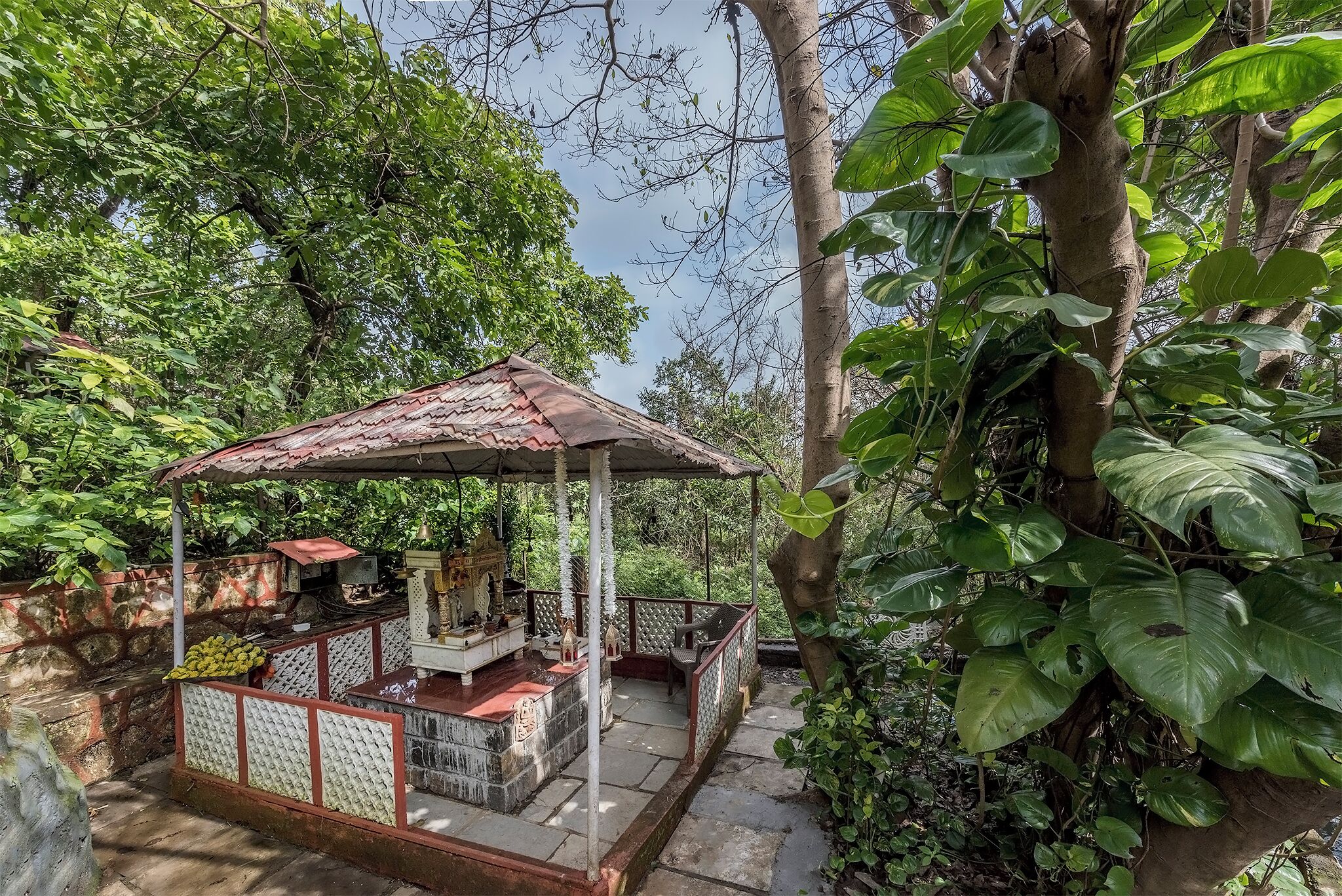 A gazebo with a tiled roof, surrounded by lush greenery and a stone wall.
