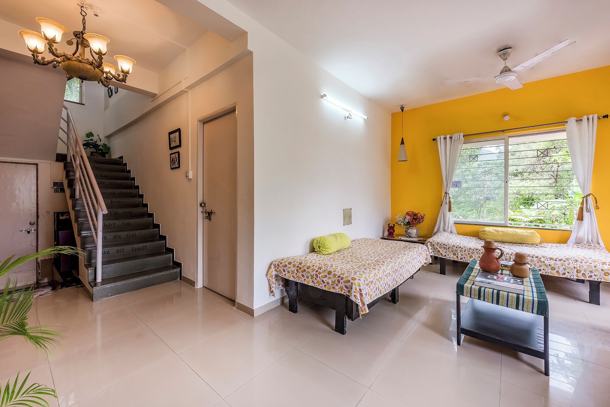 Une chambre d’hôtel avec un escalier, deux lits, une table agrémentée d’objets décoratifs et une fenêtre avec des rideaux.
