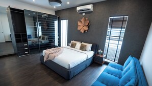 A modern bedroom with a large bed, a built-in wardrobe, a blue sofa, and a decorative wall piece. - Magnolia - 3BR Private Pool Villa (Kanakapura)