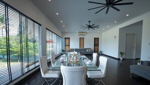 A modern dining area with a glass table, white chairs, and a view through large windows. - Magnolia - 3BR Private Pool Villa (Kanakapura)