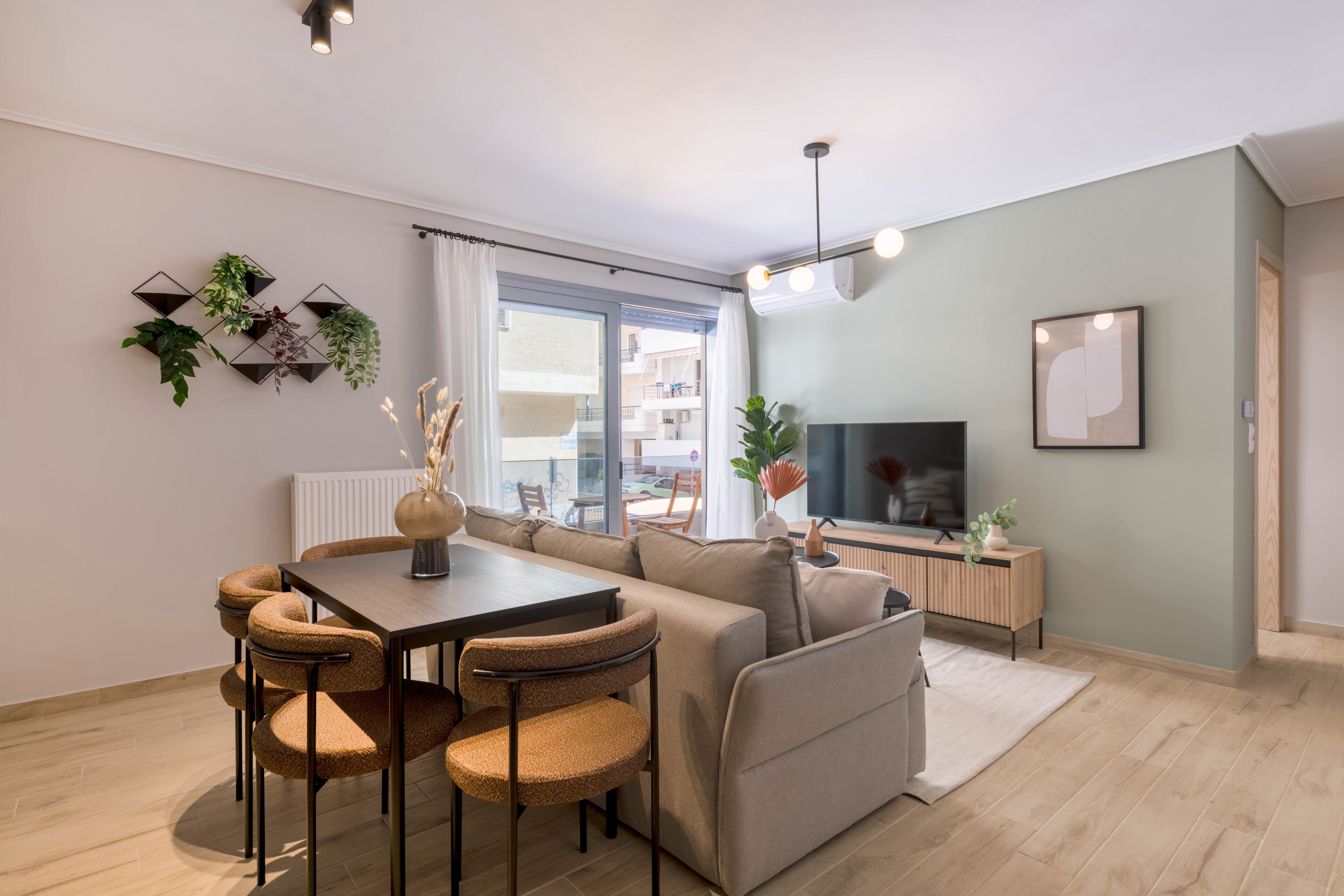 Una sala de estar moderna con sofá, mesa de comedor, sillas, televisor y ventana con vistas a edificios.