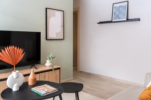 A modern living room with a flat-screen TV, a round table with a book, a decorative vase, and a plant.