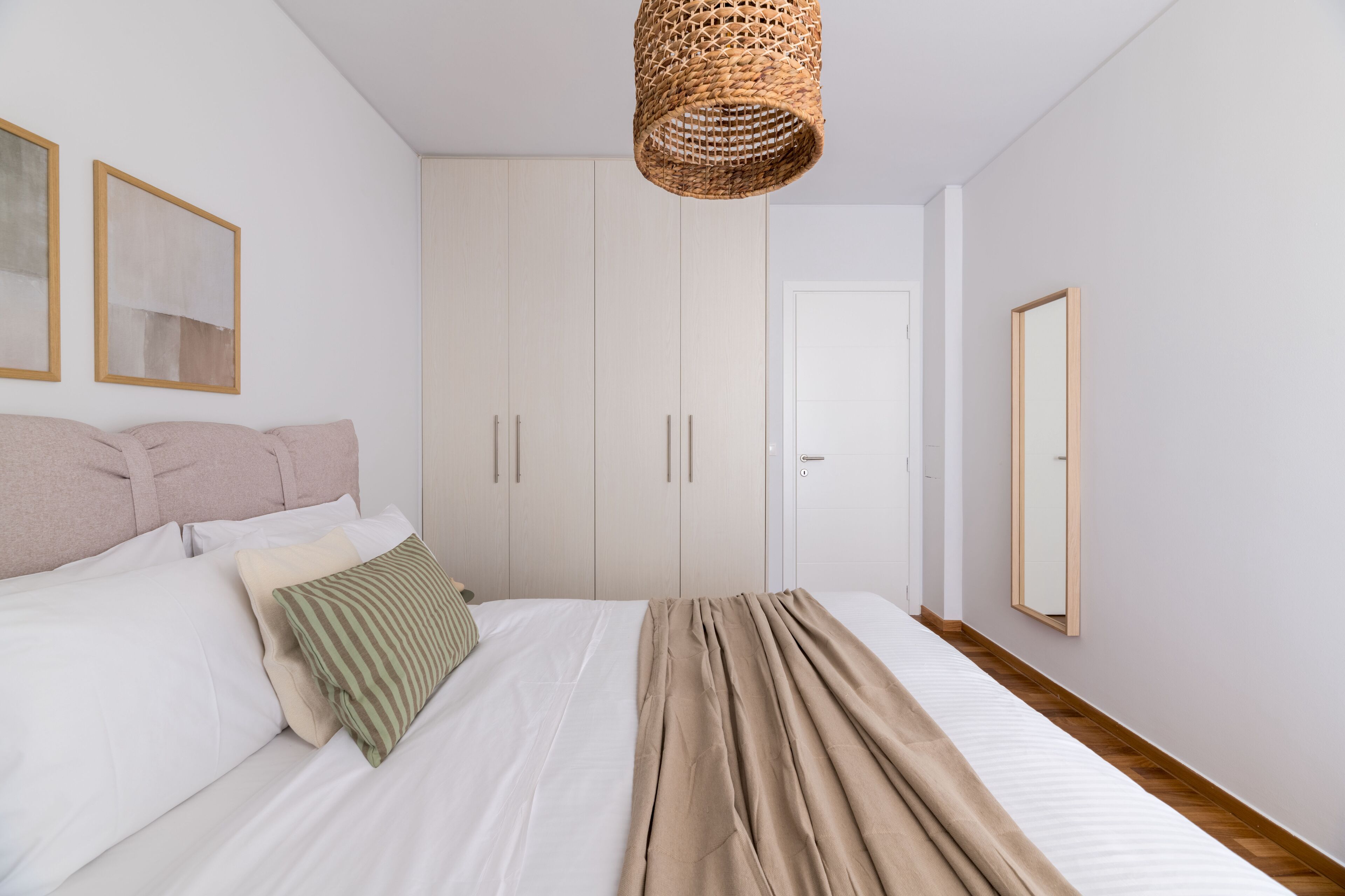 A bedroom with a bed, pillows, a hanging basket, and a wardrobe.