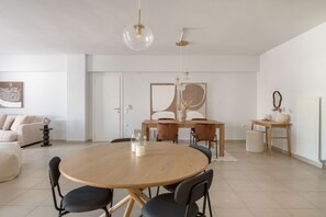A modern dining area with a round wooden table, black chairs, and a hanging light fixture. - Glistening 2BR Apartment in Marousi (Marousi)