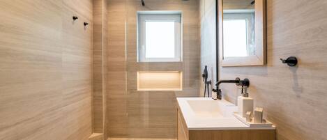 Un baño moderno con un espejo grande, una ducha y un tocador con lavamanos.