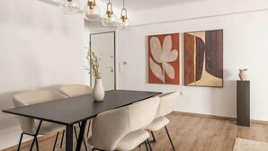 A modern dining area with a black table, white chairs, and a vase of dried flowers. There are abstract paintings on the wall and a tall black vase on a pedestal. - Prime 3BR Apartment in Ampelokipoi (Athina)