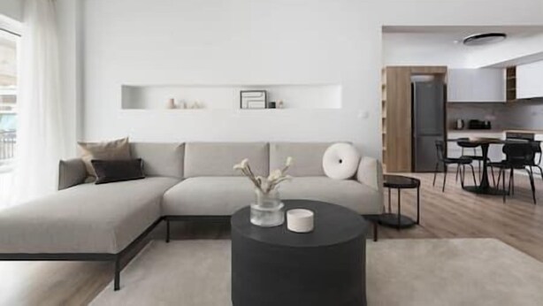 A modern living room with a sofa, a coffee table, and a kitchen area visible in the background. - Prime 3BR Apartment in Ampelokipoi (Athina)