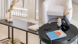 En moderne stue med en hvid sofa, et sort sofabord med en bog og en vase med tørrede planter.