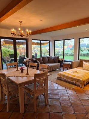 Un'ampia stanza con un tavolo da pranzo, sedie, un divano e un letto. Grandi finestre offrono vista sull'esterno.