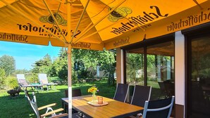 An outdoor patio area with a table and chairs under a yellow umbrella, surrounded by brick flooring and greenery. - Romantic house with sauna and fireplace near the lake (Zossen)