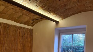 A cozy bedroom with two beds, a window with a view of greenery, a wooden ceiling, and a bedside table with a lamp. - Romantic house with sauna and fireplace near the lake (Zossen)