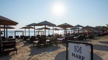 Une plage avec des transats et des parasols, un panneau indiquant « Mare », et une vue dégagée sur la mer.