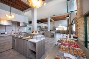 A modern kitchen with a buffet setup, featuring a central island with food and a variety of dishes displayed on the counter. - Mare Village Hotel (Apokoronas)