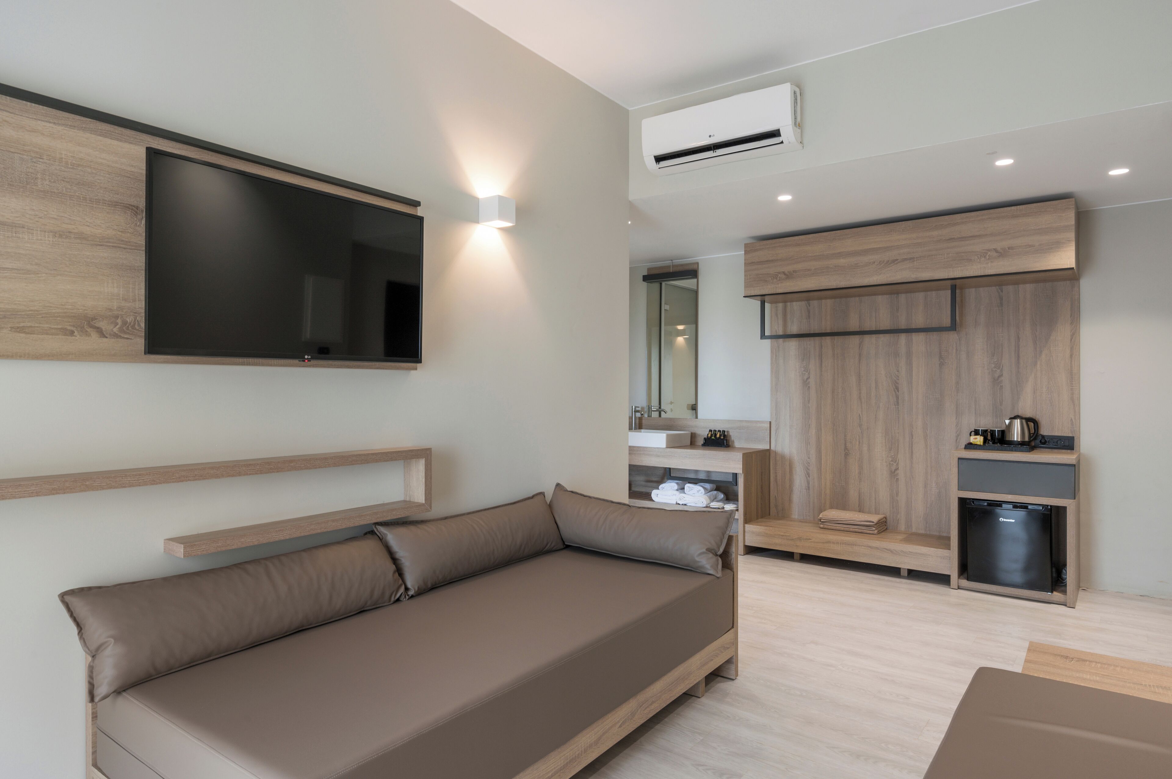 Una sala de estar moderna con un sofá, un televisor de pantalla plana montado en la pared y una cocina integrada con un fregadero y espacio de almacenamiento.
