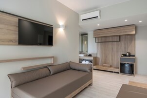 Una sala de estar moderna con un sofá, un televisor de pantalla plana montado en la pared y una cocina integrada con un fregadero y espacio de almacenamiento.