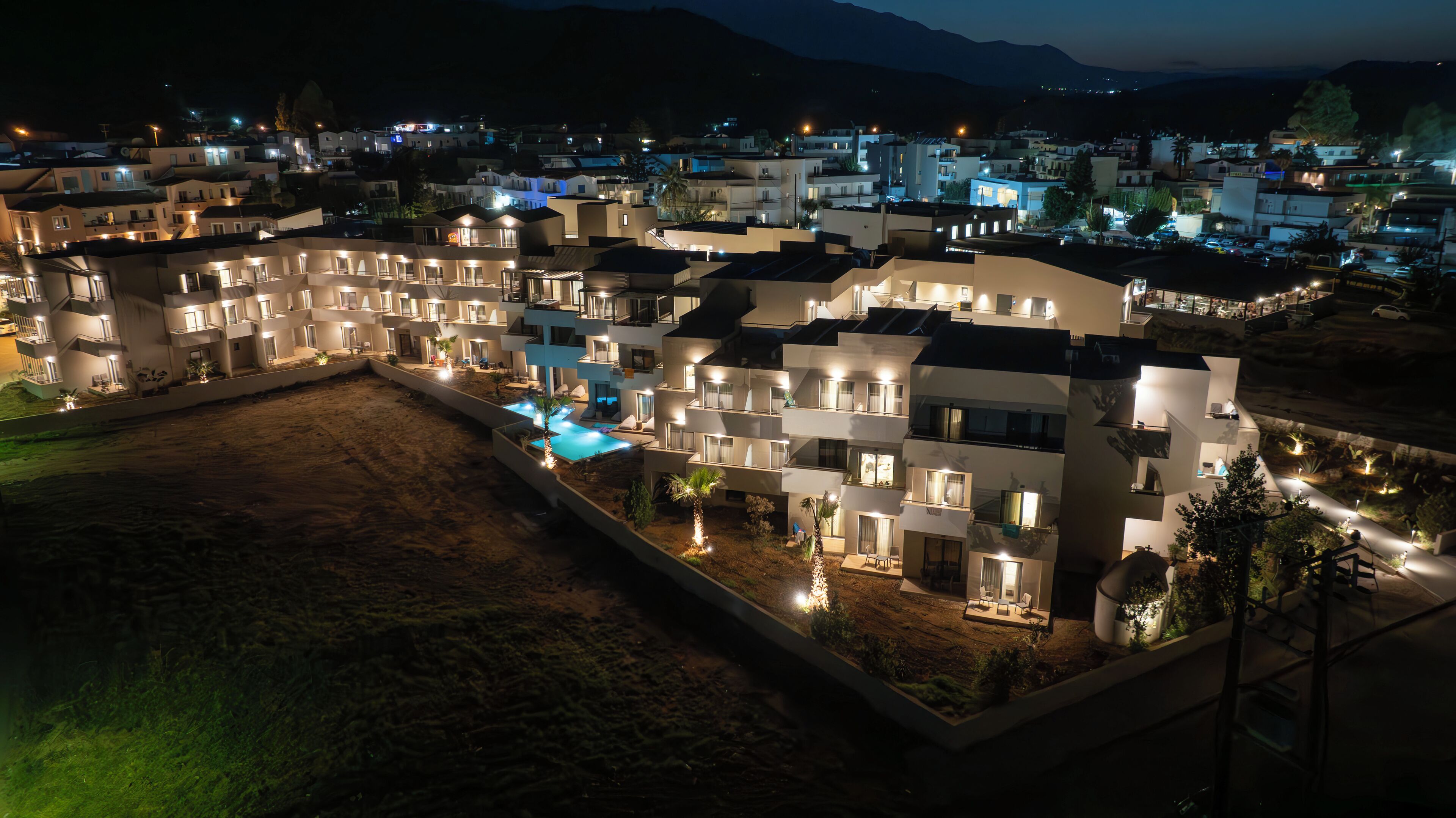 Un hotel moderno con diversi piani, una piscina e una zona esterna ben illuminata.