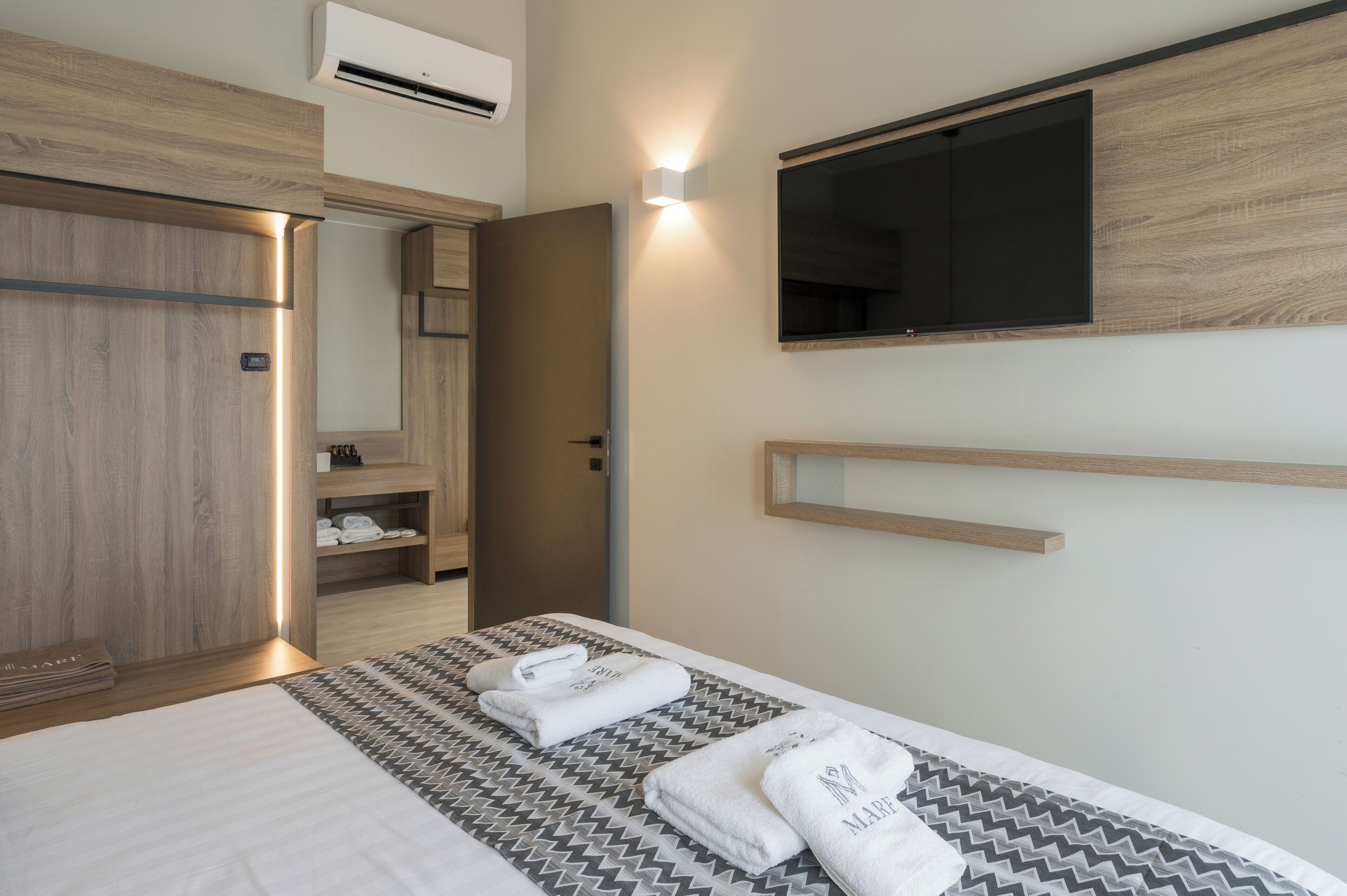 Una habitación de hotel moderna con una cama grande, un armario empotrado, un televisor de pantalla plana en la pared y una pequeña estantería.