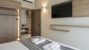 Una habitación de hotel moderna con una cama grande, un armario empotrado, un televisor de pantalla plana en la pared y una pequeña estantería.