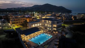 Ein modernes Hotel mit Dachpool, mehreren Balkonen und Blick auf Meer und Berge.