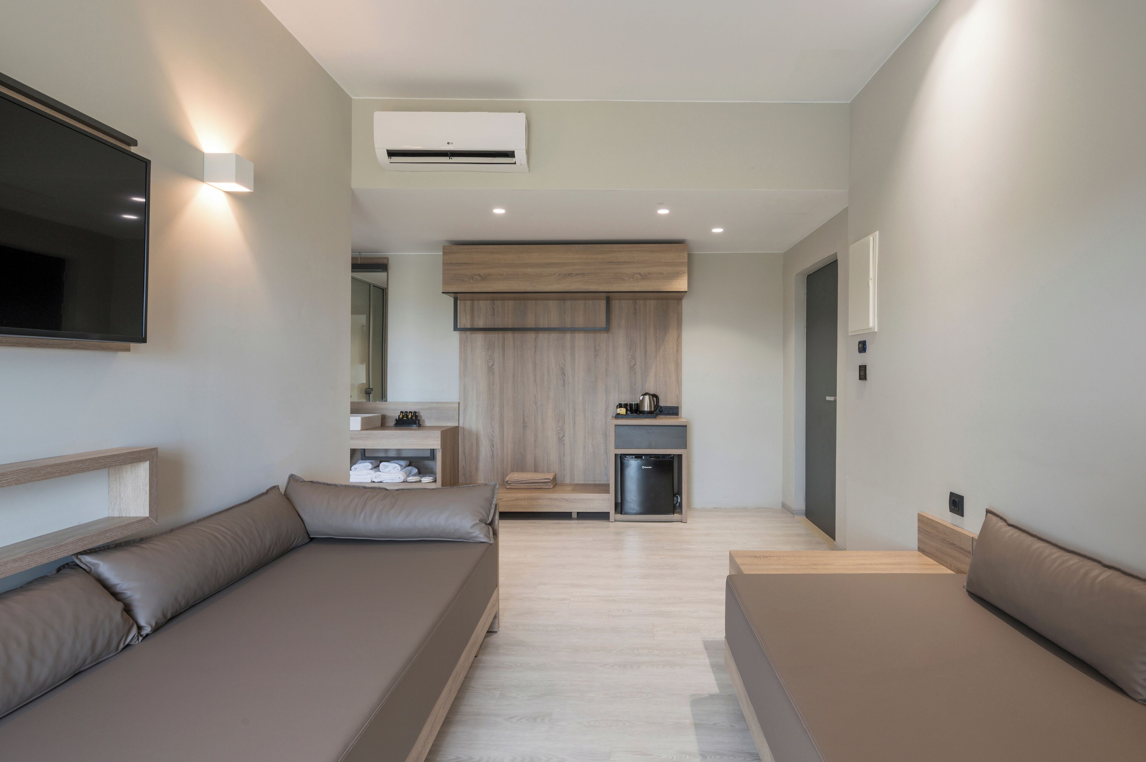 Una habitació d'hotel moderna amb sofà, una cuineta petita, televisió i una paret decorativa de fusta.