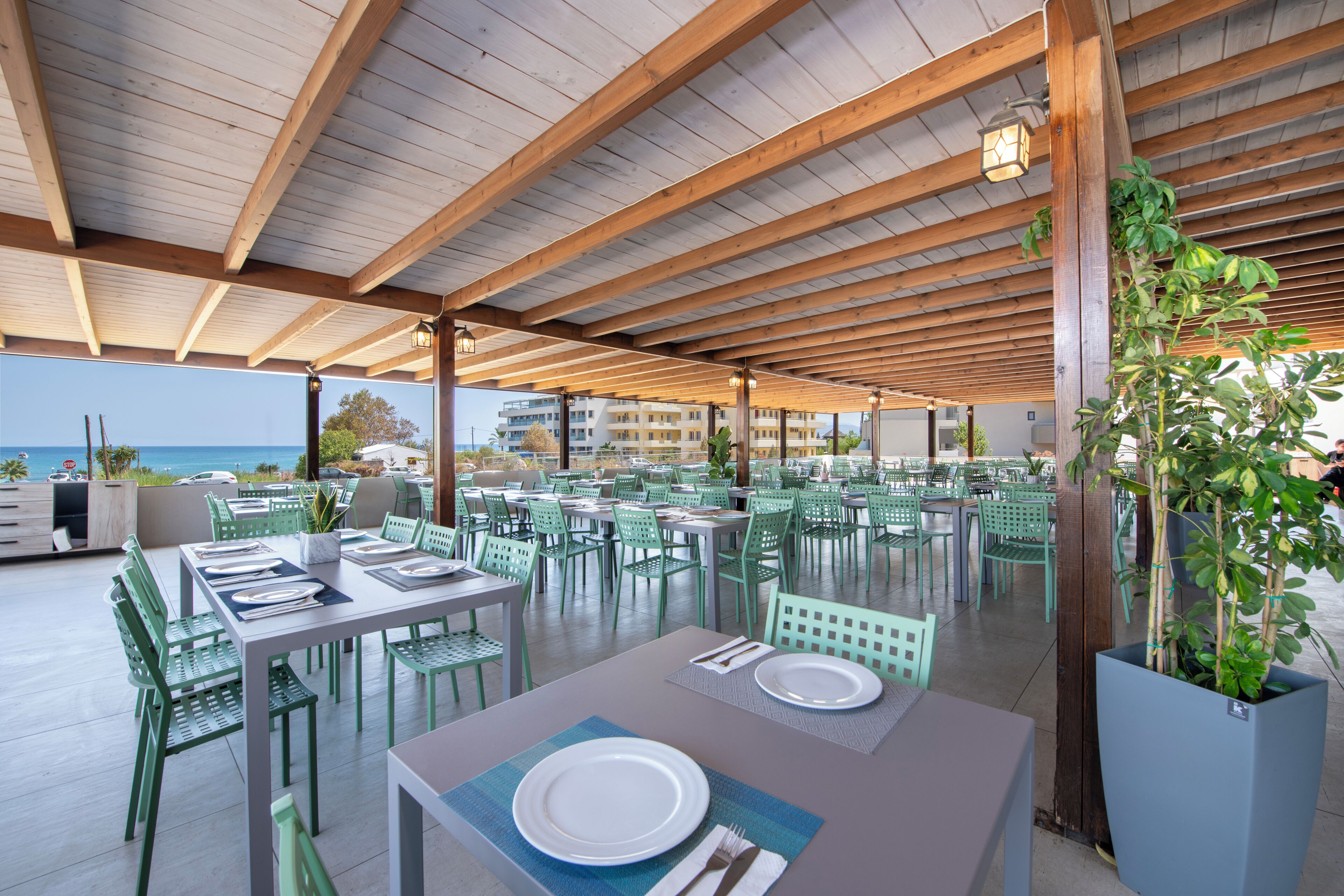 An outdoor dining area with green chairs and tables, wooden beams, and a view of the ocean.
