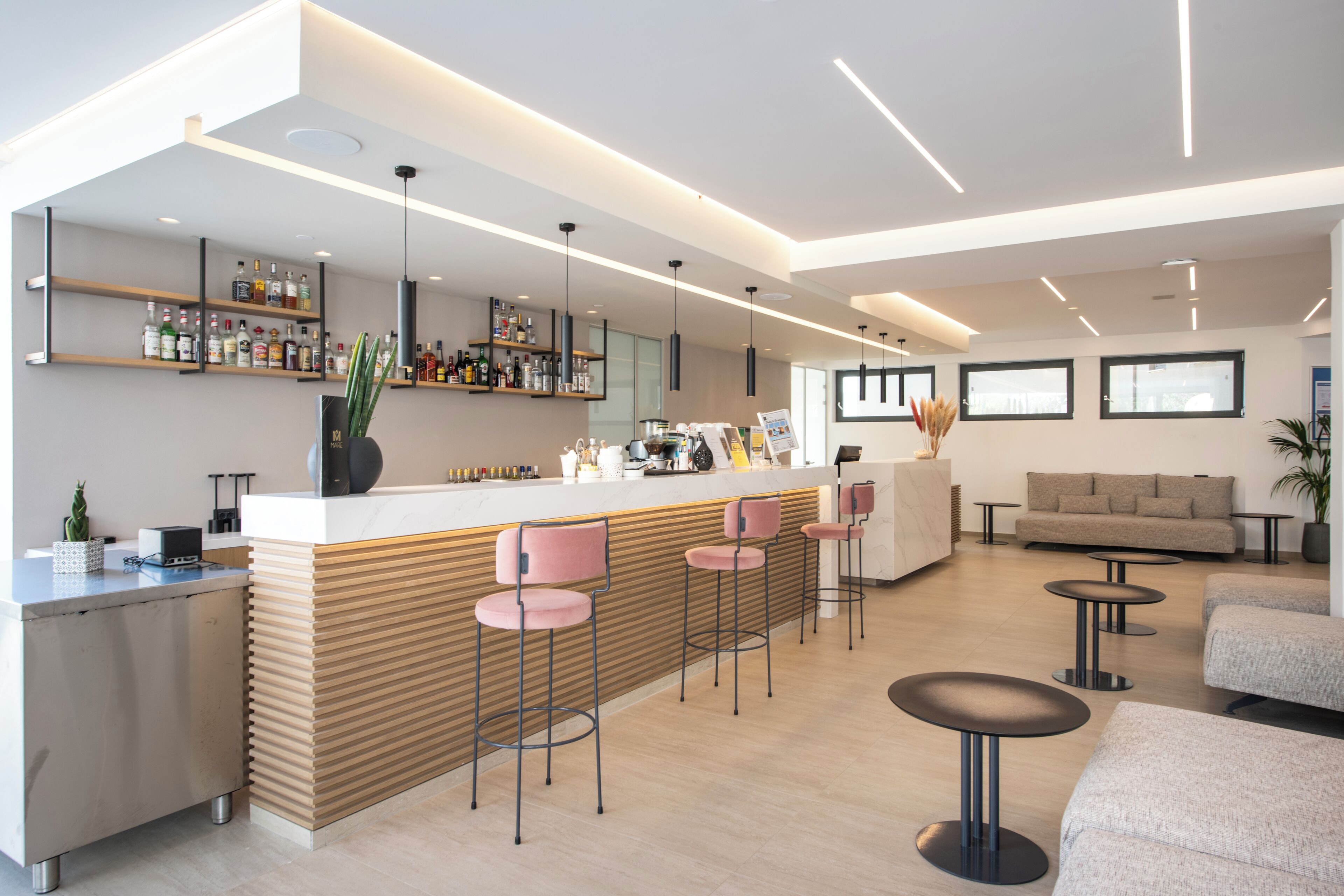 Eine moderne Bar mit einer Theke, Barhocker und Flaschenregalen. Es gibt Sitzbereiche mit Sofas und runden Tischen.