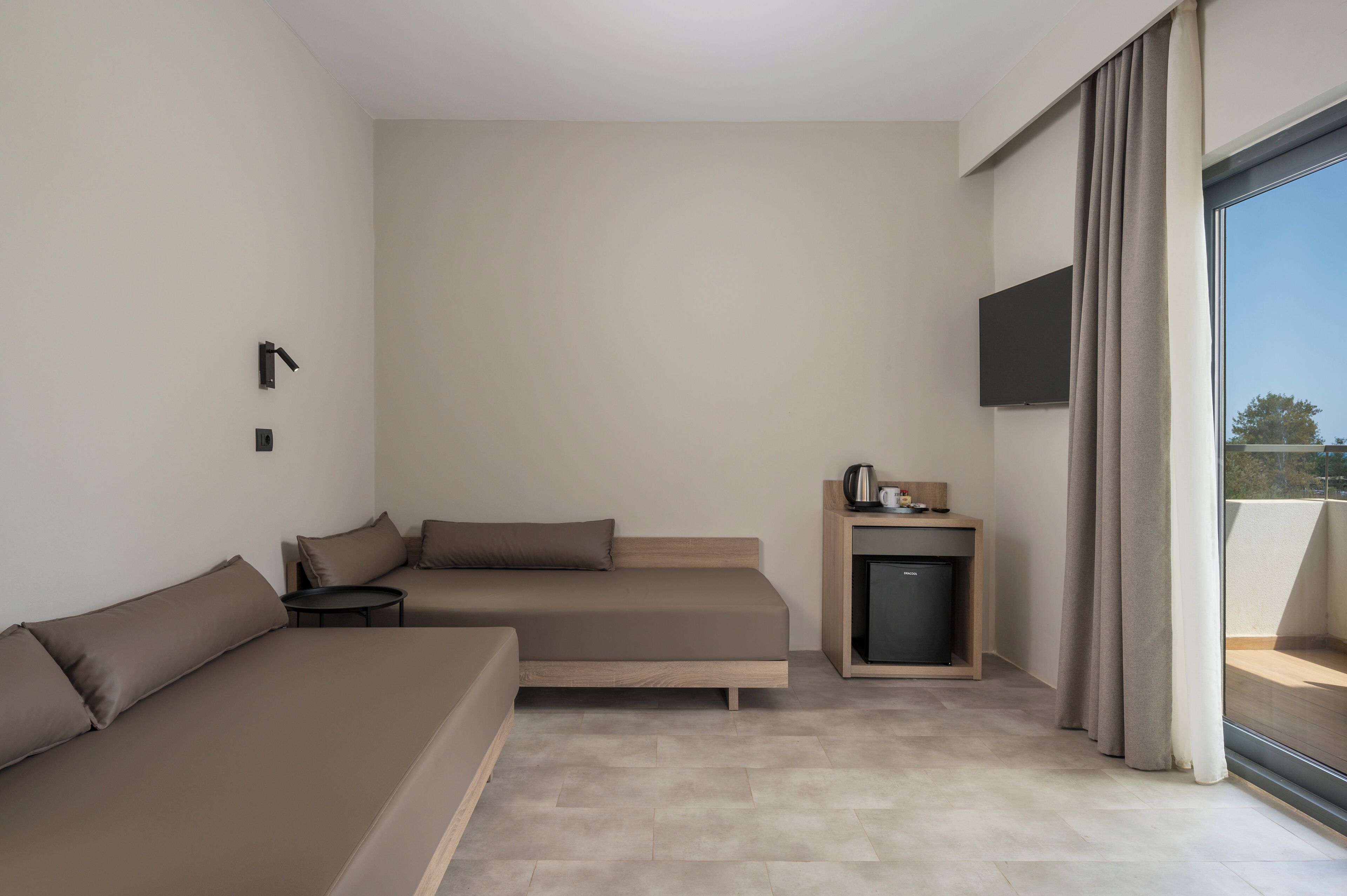 A modern hotel room with a sofa, a small table, a TV, and a mini-fridge.