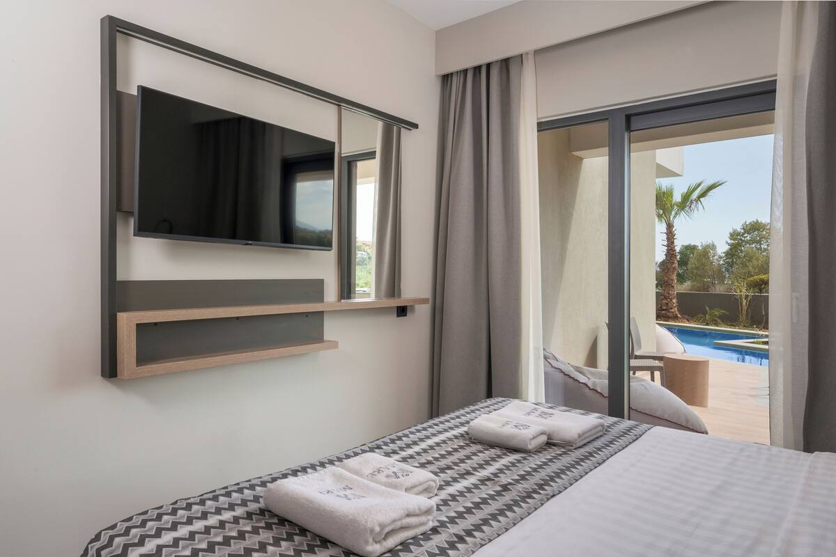 A hotel room with a bed, a mounted TV, and a view of an outdoor pool.