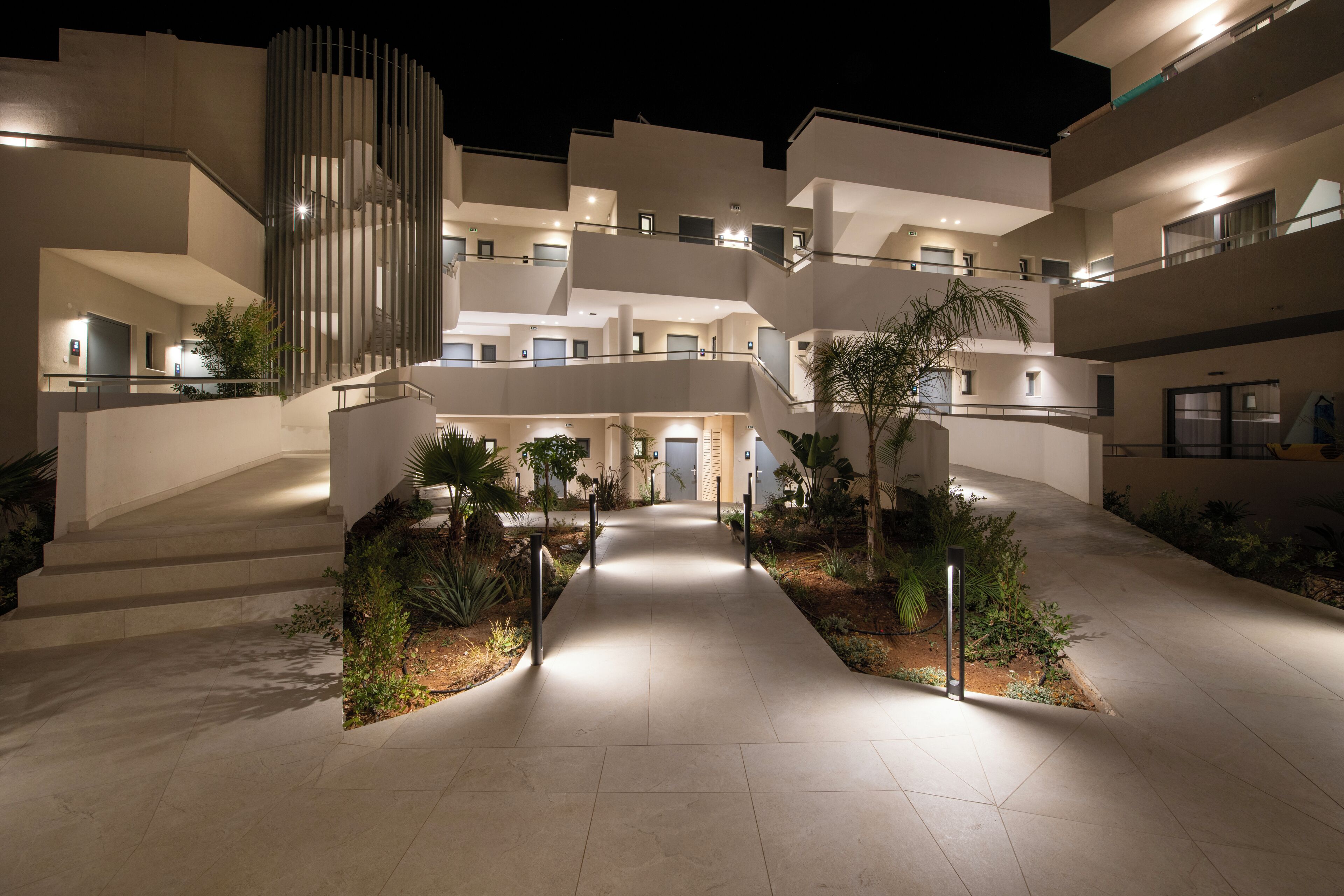 A modern hotel with multiple floors, a central courtyard with plants, and a well-lit entrance.