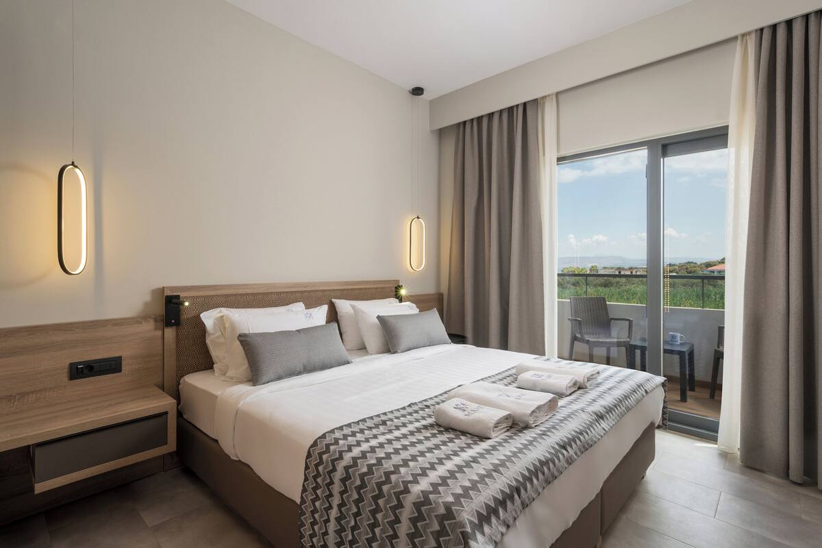 A hotel room with a large bed, a nightstand, a desk, and a balcony with a view.