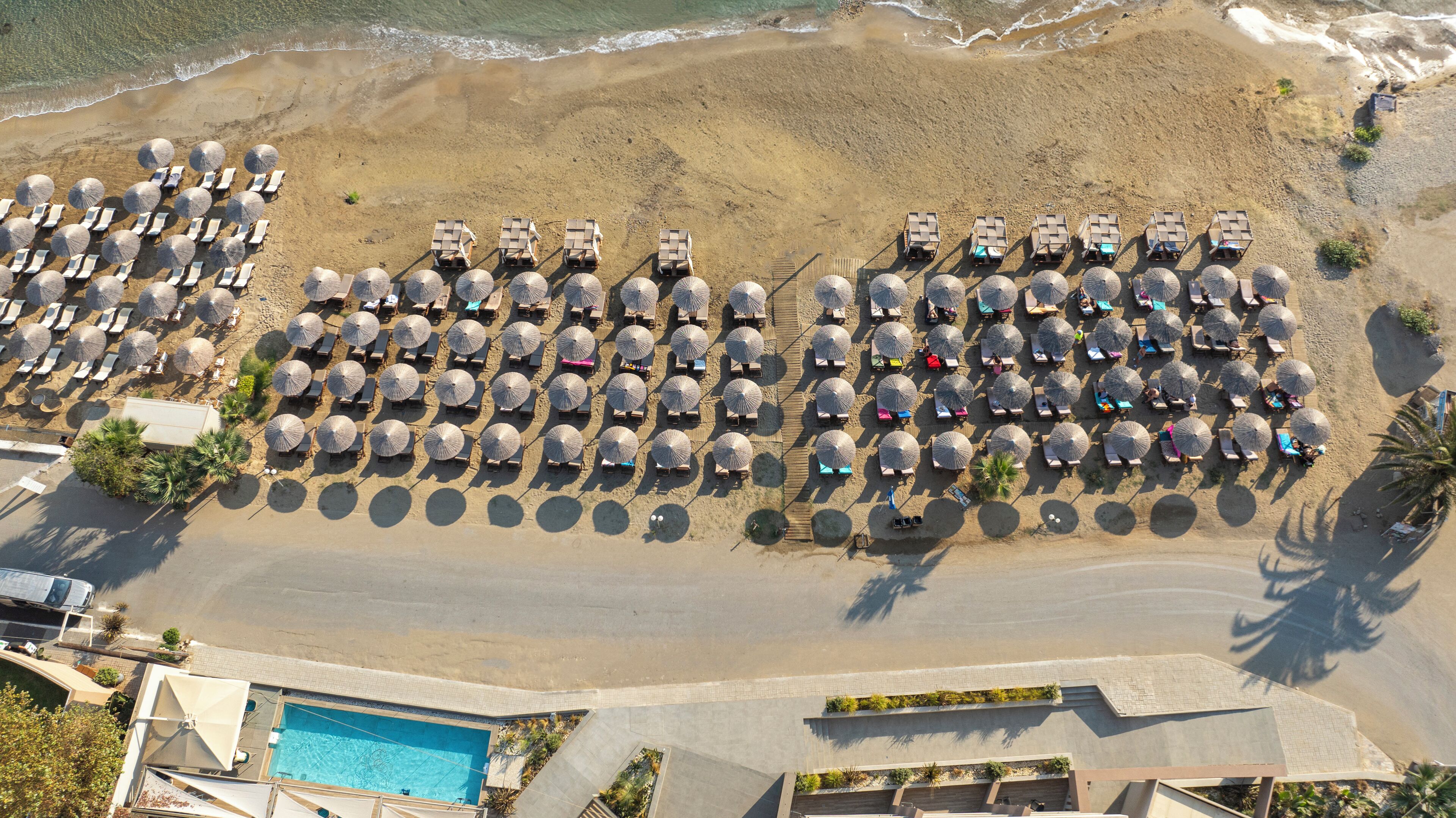 Eine Vogelperspektive eines Strandresorts mit Liegestühlen und Sonnenschirmen, einem Pool und einem Sandstrand.