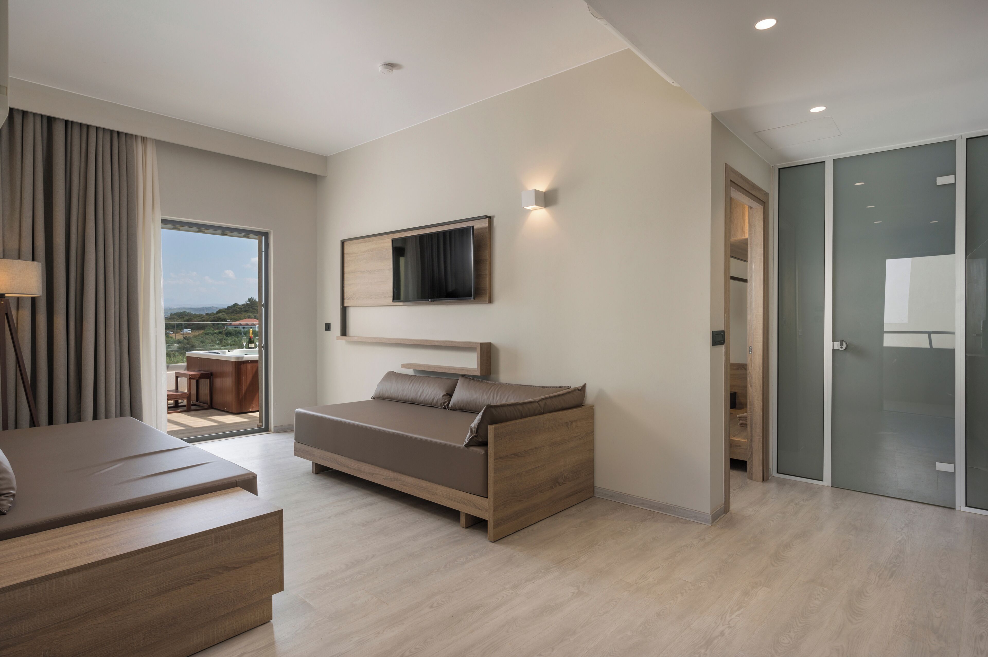 A modern bedroom with a bed, a TV mounted on the wall, and a balcony with a view.