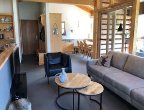 A cozy living area with a sofa, a chair, and a coffee table. There is a kitchen in the background with wooden cabinets and a dining table. - Austrian Valley Chalet Retreat (Wald im Pinzgau)