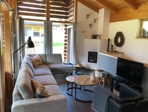 Moderni olohuone, jossa on kulmasohva, pyöreä sohvapöytä, litteänäyttöinen televisio ja takka.
