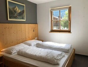 Habitació amb capçal de fusta, llit amb roba de llit blanca, finestra amb vista a vegetació i un quadre a la paret.