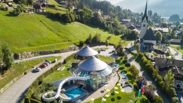 Un resort con piscina, una zona techada e iglesia al fondo.