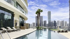Una piscina en la azotea con sillones de descanso, una palmera y un horizonte urbano de fondo.