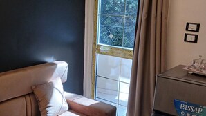 Une pièce avec un canapé beige, une petite table sur laquelle se trouvent une carafe et des verres, et une fenêtre avec des rideaux.