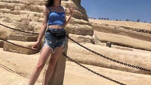 Une personne se tient devant une grande structure en pierre, avec une pyramide en arrière-plan.