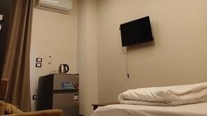 Une chambre d’hôtel équipée d’un lit, d’un bureau, d’un réfrigérateur et d’un téléviseur à écran plat fixé au mur.