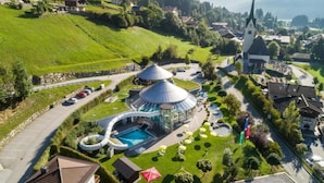 A resort with a pool, a dome-shaped building, and a church in the background. - Spacious Detached Chalet in Holiday Village (Wald im Pinzgau)