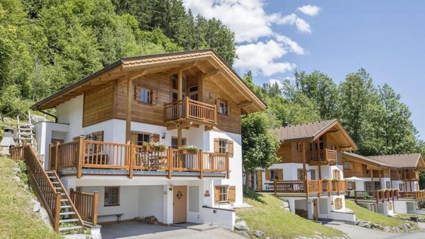 A wooden chalet with a balcony, a staircase, and a view of the surrounding forest. - Spacious Detached Chalet in Holiday Village (Wald im Pinzgau)