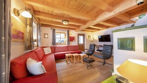 A cozy living room with a red sofa, a black chair, a small table, and a television on the wall. - Spacious Detached Chalet in Holiday Village (Wald im Pinzgau)