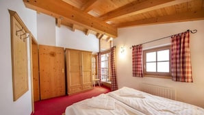 A bedroom with a wooden ceiling, a bed with white bedding, a window with plaid curtains, and a red carpet. - Spacious Detached Chalet in Holiday Village (Wald im Pinzgau)