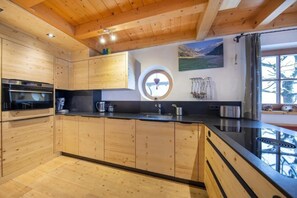 Eine moderne Küche mit Holzschränken, einer schwarzen Arbeitsplatte und Blick ins Freie durch ein Fenster.
