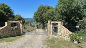 A gated entrance with stone walls and a metal gate, surrounded by trees and a clear sky.