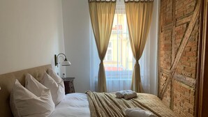A hotel room with a bed, pillows, a blanket, a lamp, and a view through a window with curtains.