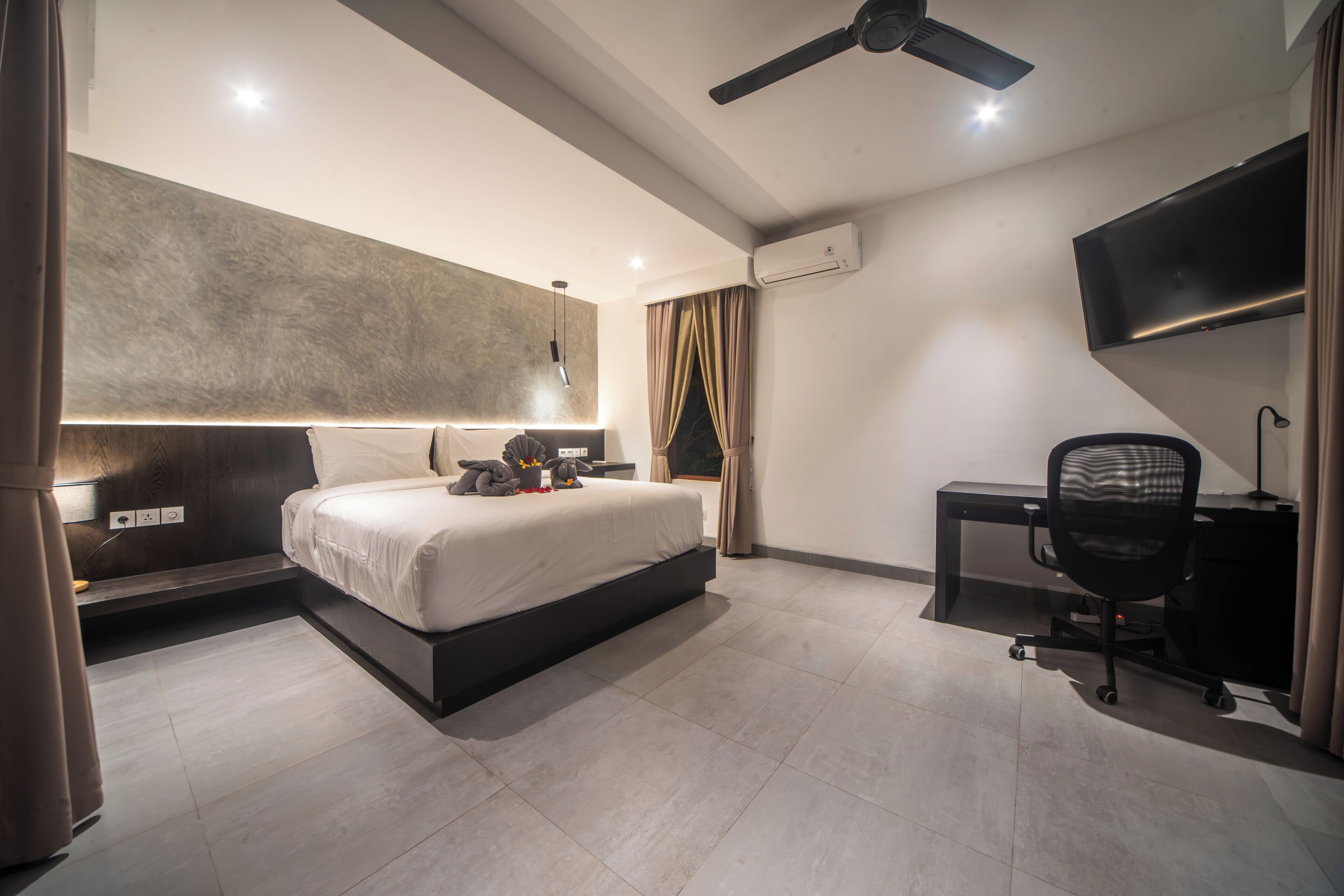 Ein modernes Hotelzimmer mit einem großen Bett, einem Schreibtisch, einem Sessel, einem Deckenventilator und einem Fernseher.