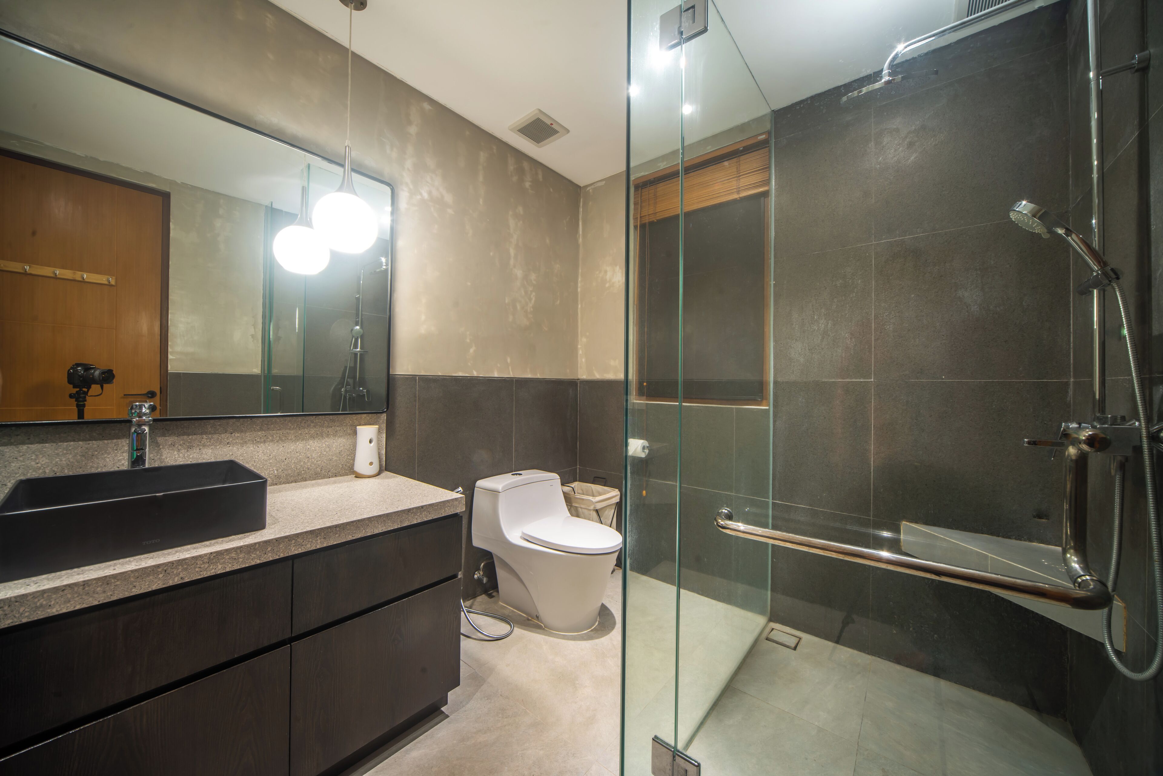 Een moderne badkamer met een douchecabine van glas, een grote spiegel en een donkere wastafelmeubel.