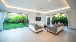 A spacious living room with a large window, a ceiling fan, and a flat-screen TV. - Luxury 4 Bedroom Bella Vista Villa (Ungasan)